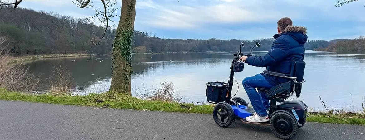 Mann fährt mit E-Scooter Scuddy Premium QUAD am See Mann fährt mit E-Scooter Scuddy Premium QUAD am See